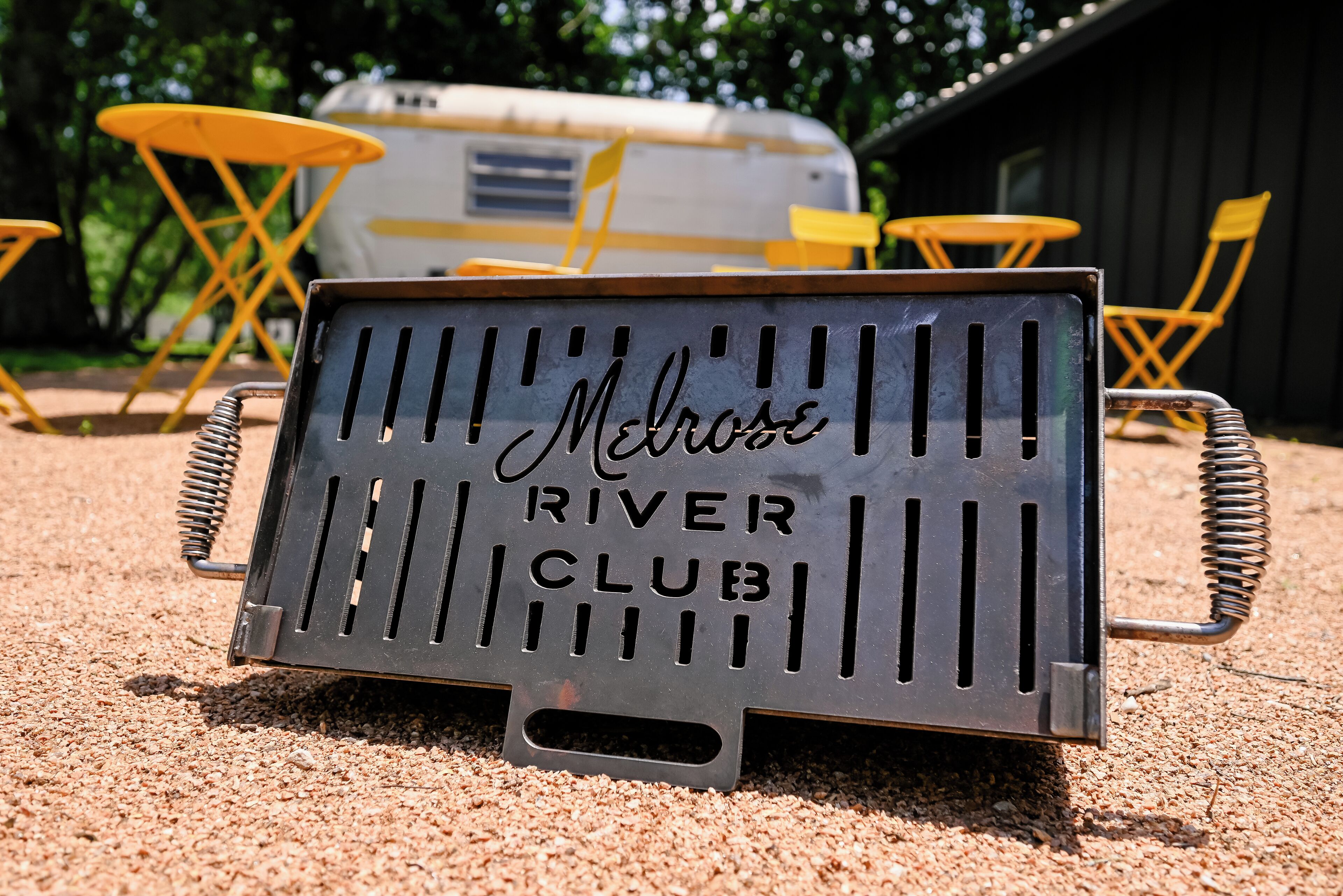 A metal sign with the text "Melrose River Club" on a gravel surface.