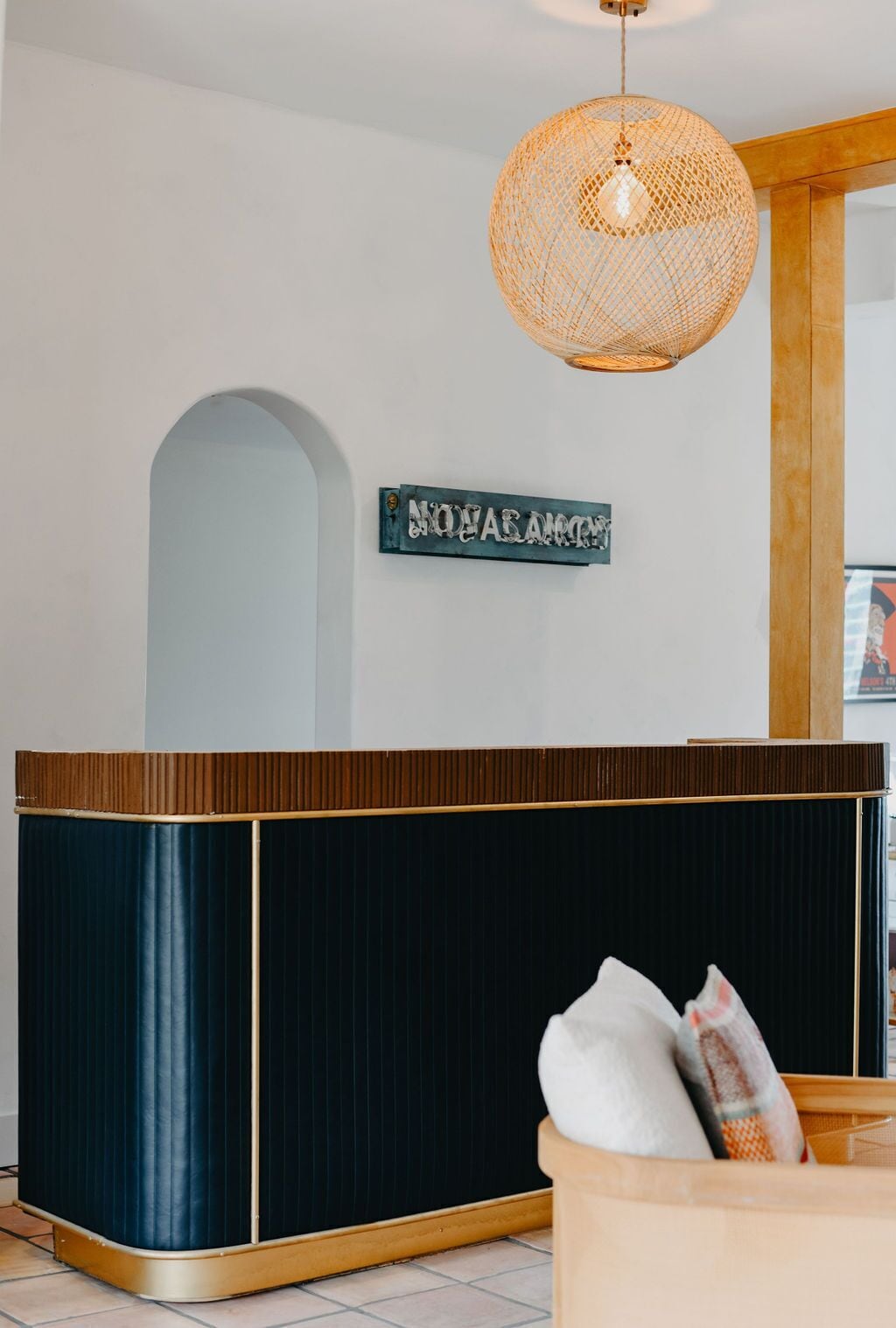 A reception desk with a dark finish, a woven light fixture above, and a sign with text.