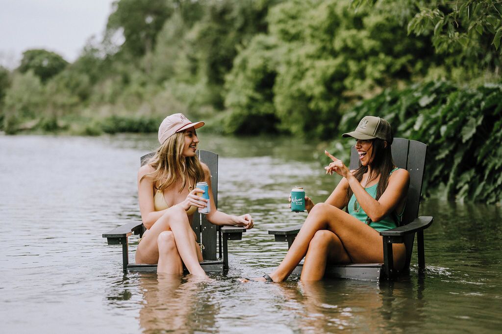 Two people sitting on chairs in a body of water, surrounded by greenery.
