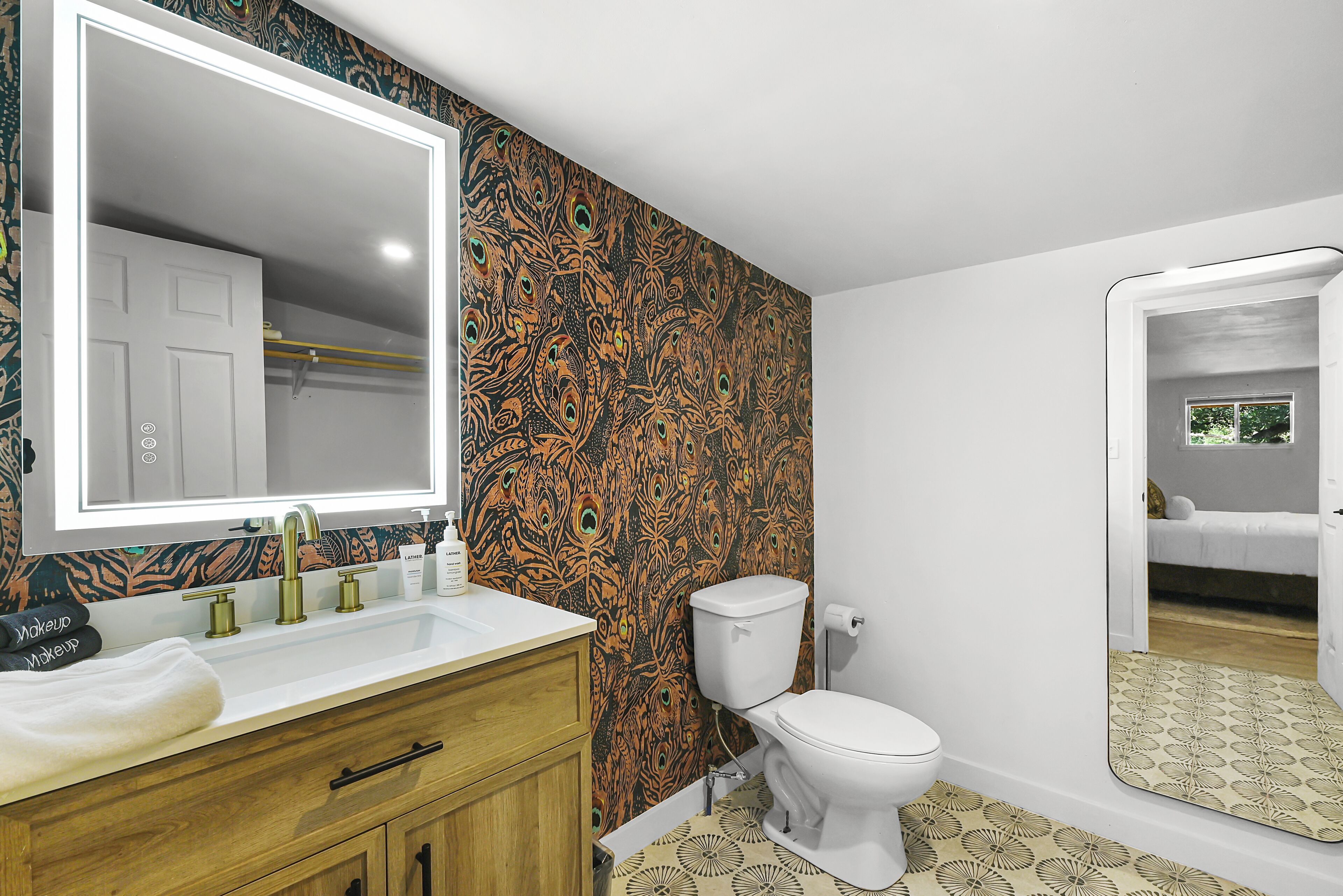 Un baño con inodoro blanco, lavabo con espejo y pared con diseño.