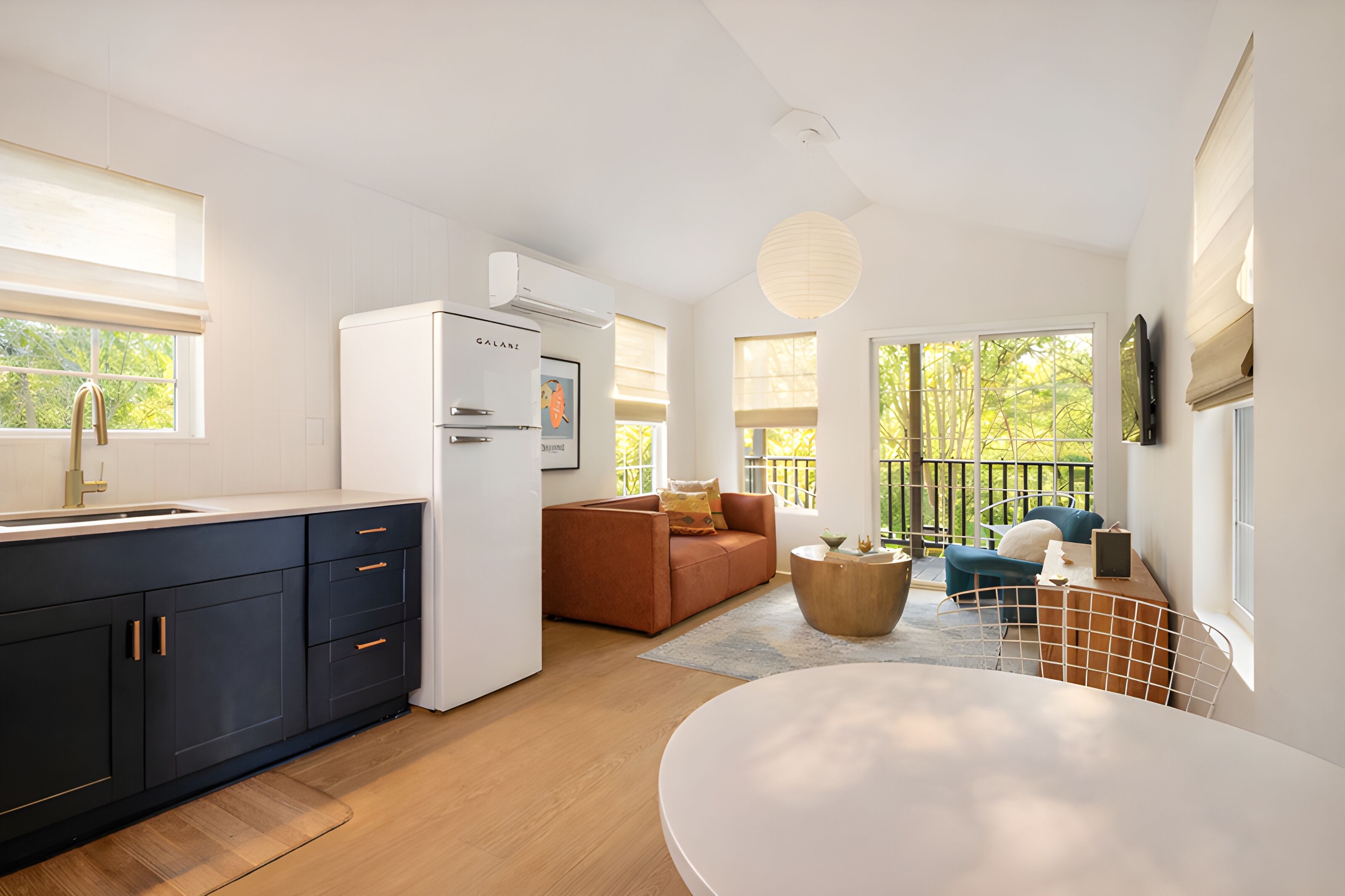 A modern kitchen with a refrigerator, a dining area with a round table, and a living space with a sofa and a TV.