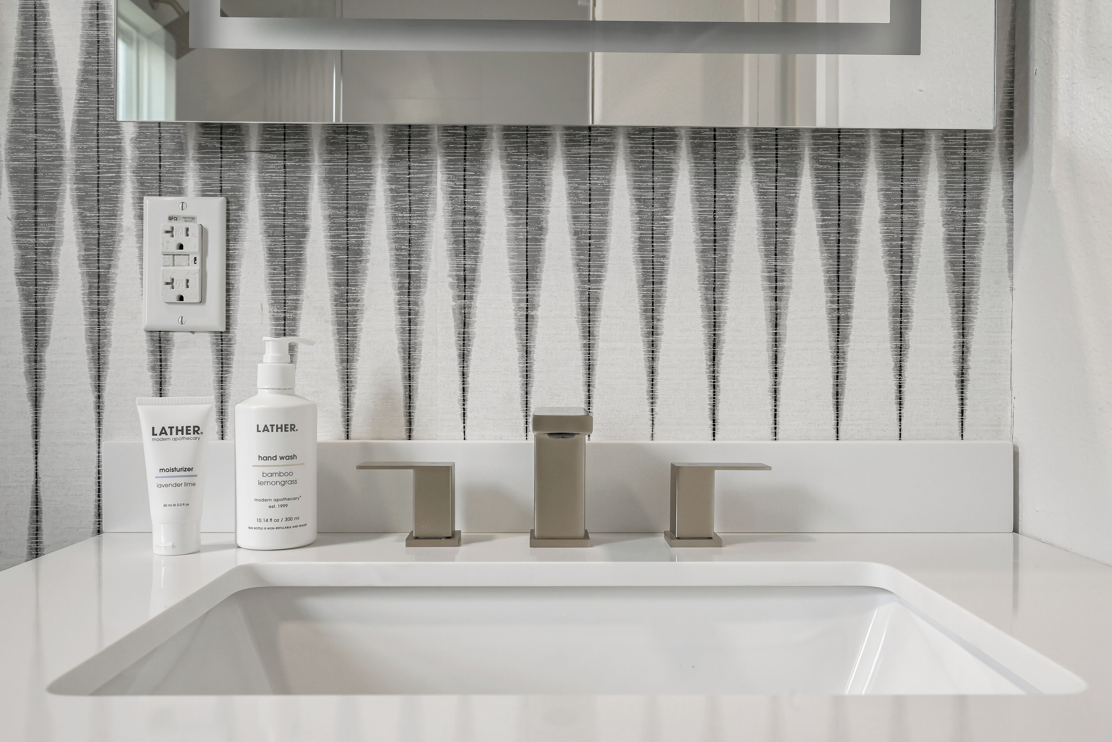 A bathroom with a white sink, two Lather hand wash bottles, and a modern faucet.