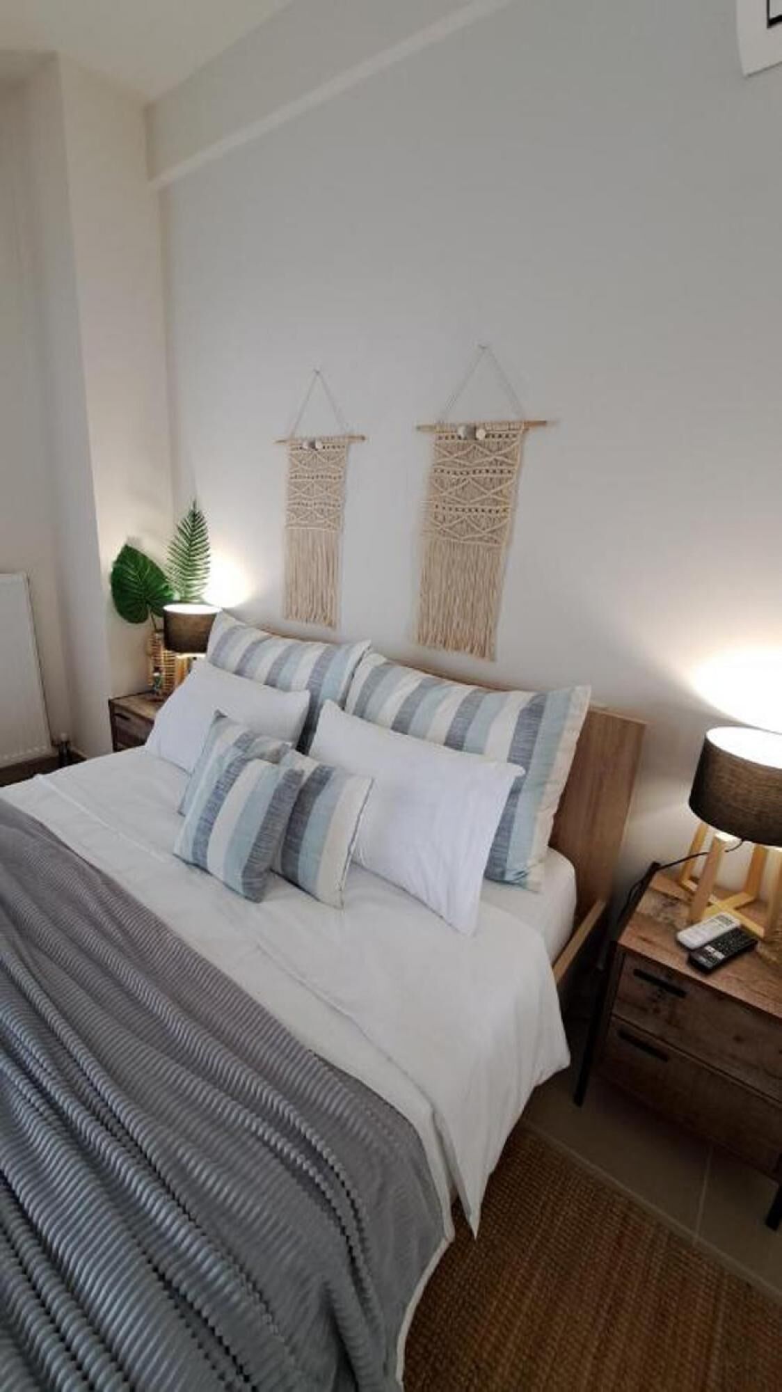 A bedroom with a bed, two nightstands, a lamp, and macramé wall hangings.