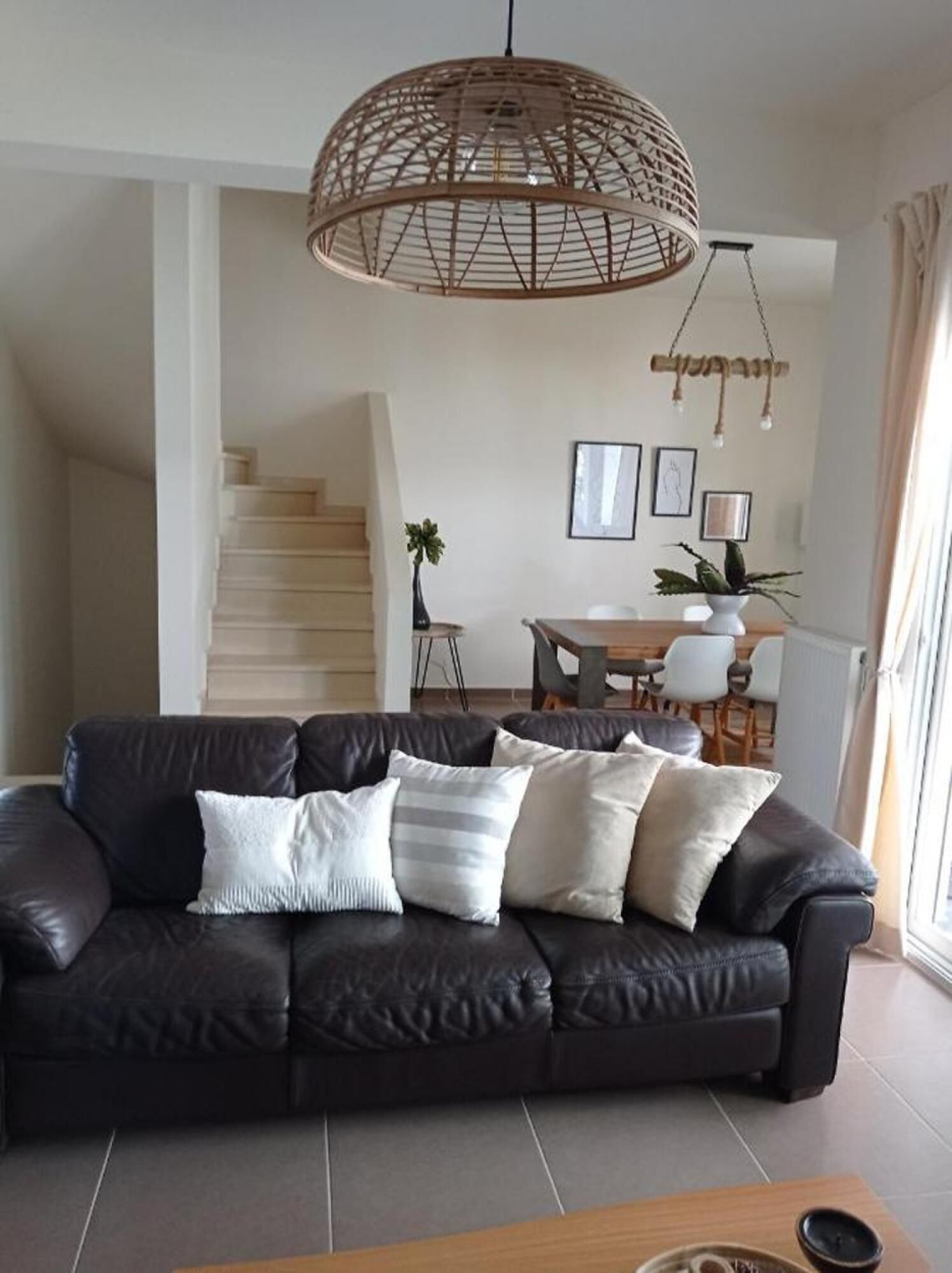 Una sala de estar moderna con un sofá de cuero negro, una mesa de centro de madera y una lámpara colgante.