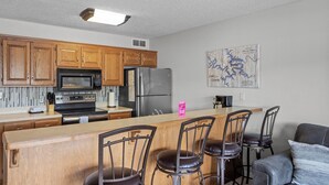 Una cocina con armarios de madera, un refrigerador de acero inoxidable, un microondas y una zona de bar con sillas.