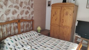 Ein Schlafzimmer mit einem Bett, einem Holzschrank, einem Nachttisch, einer Lampe und einem Fernseher.