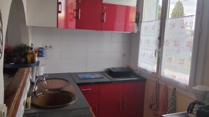 Eine Küche mit roten und weißen Schränken, einem Spülbecken, einem Fenster mit floralem Rollo sowie einer Arbeitsplatte mit Wasserkocher und Küchengerät.