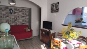 Ein Wohnzimmer mit einem roten Sofa, einem Fernseher auf einem Holzboden, einem Esstisch mit Stühlen und einer Wand mit gerahmten Bildern.