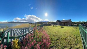 A scenic view of a property with a grassy area, a wooden deck, and a building with a sloped roof. - LA 48 (El calafate)