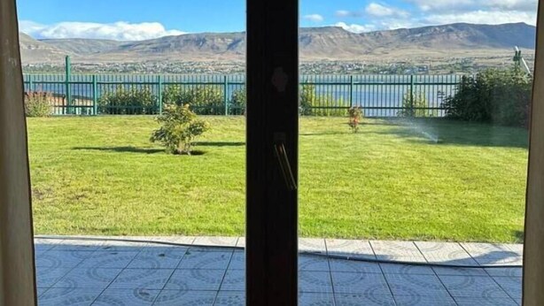 A room with a large sliding glass door leading to a balcony with a view of a grassy area, a fence, and mountains in the distance. - LA 48 (El calafate)