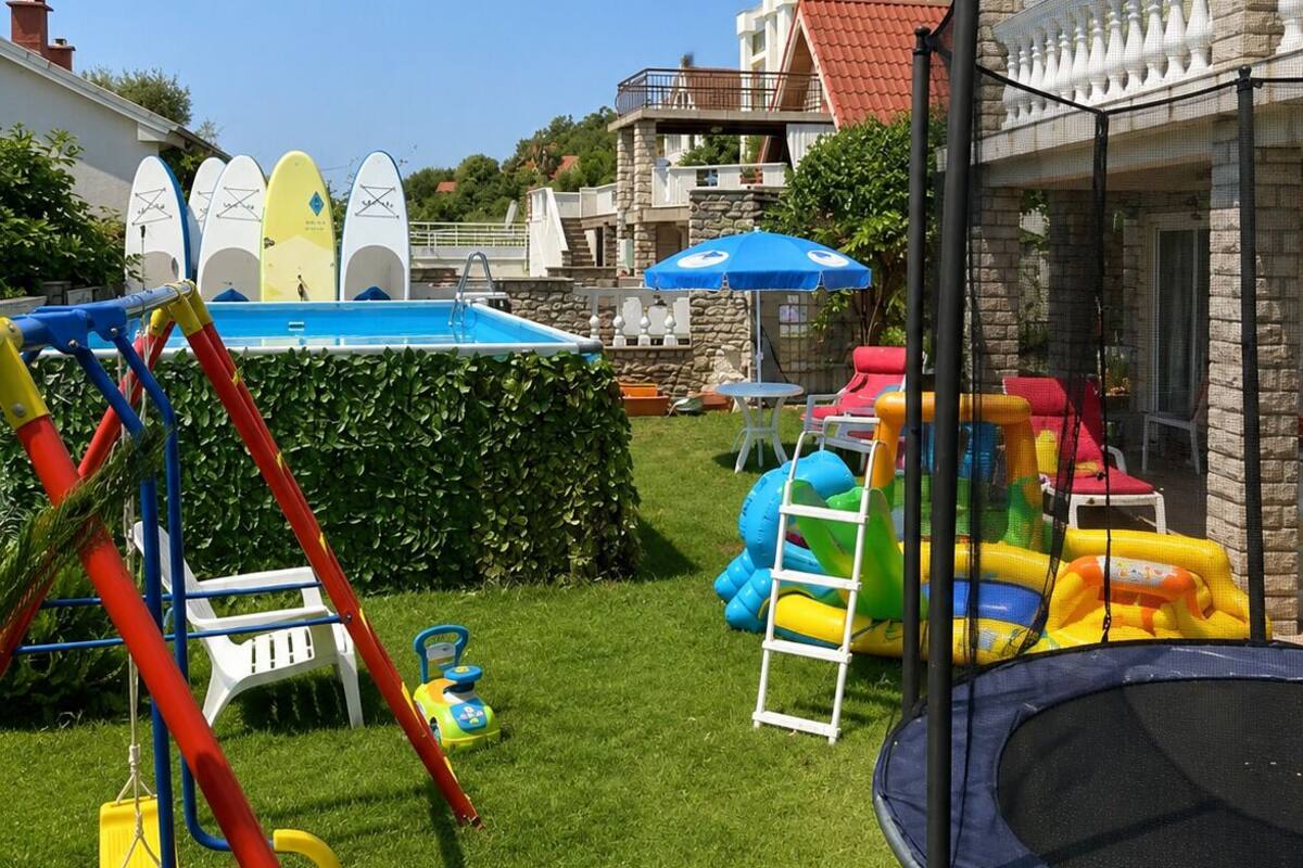Un patio trasero con un trampolín, estructuras de juego inflables, una piscina y un columpio.