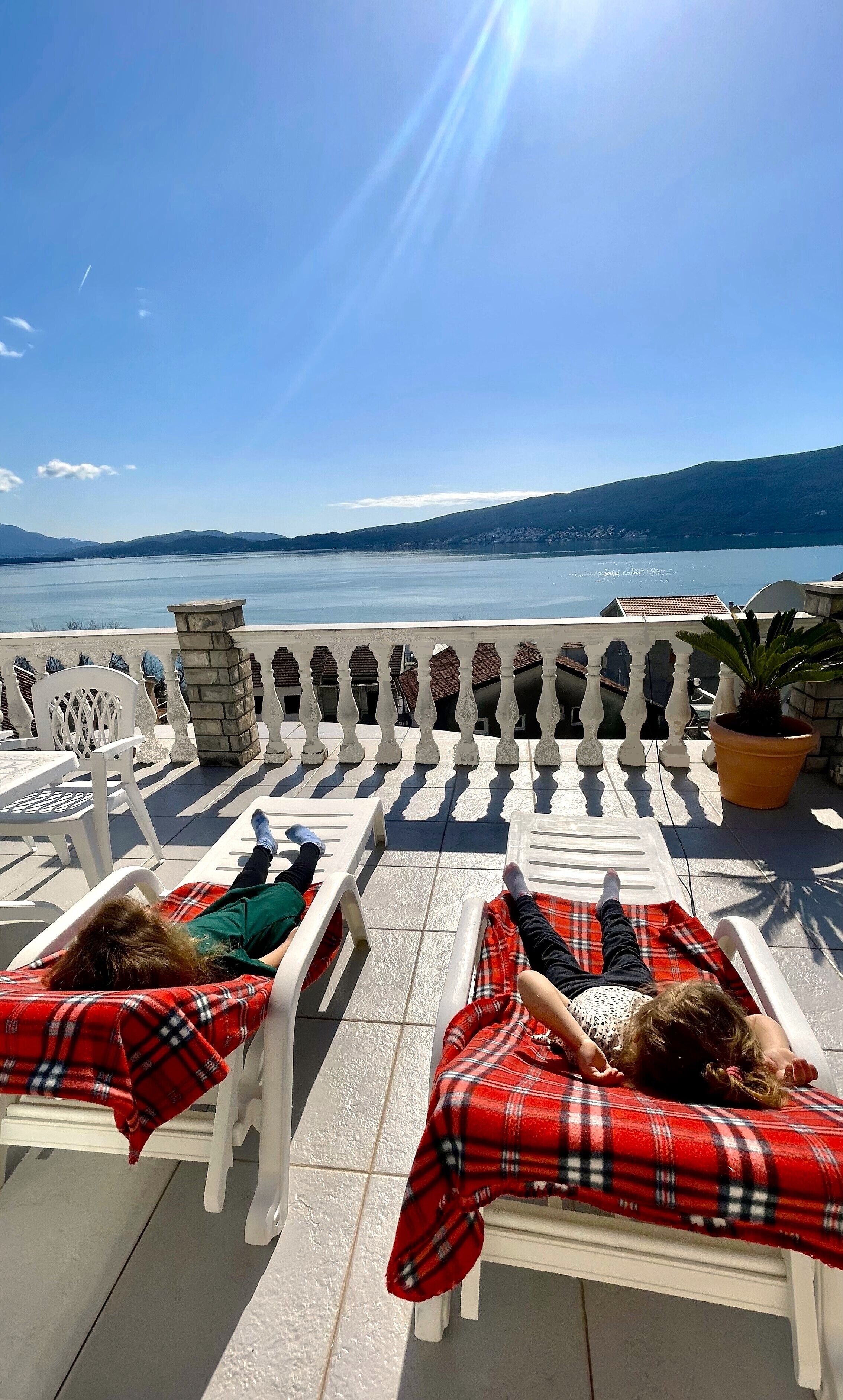 Un balcón con dos sillones de descanso, una planta en maceta y vistas a un cuerpo de agua y montañas.