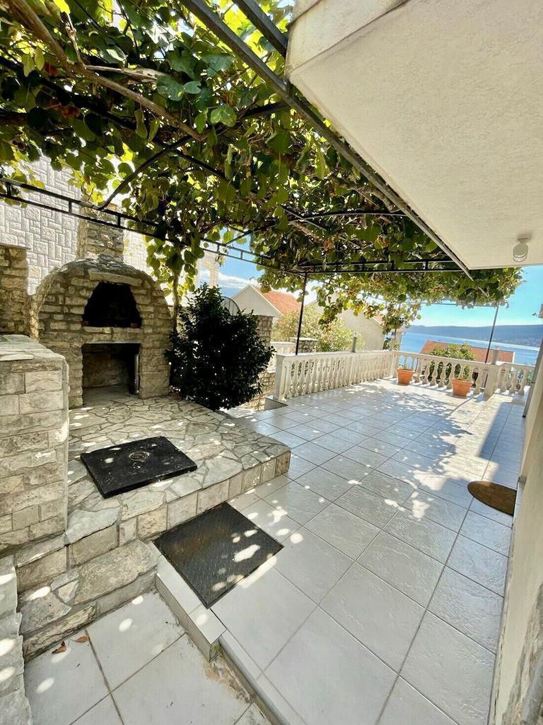A stone-built outdoor area with a brick oven, tiled flooring, and a view of the sea.