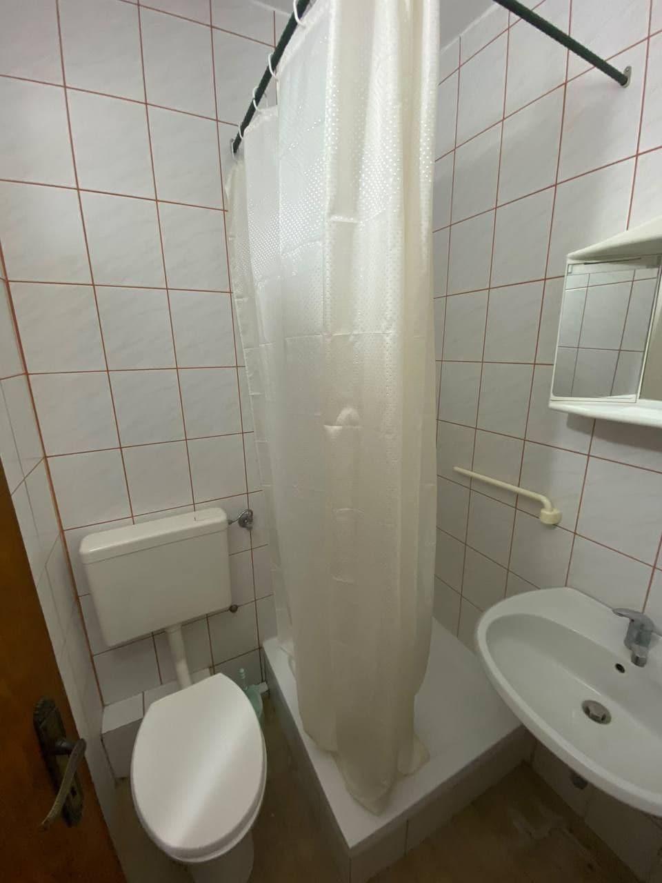 A bathroom with a toilet, a shower with a curtain, and a sink with a mirror.