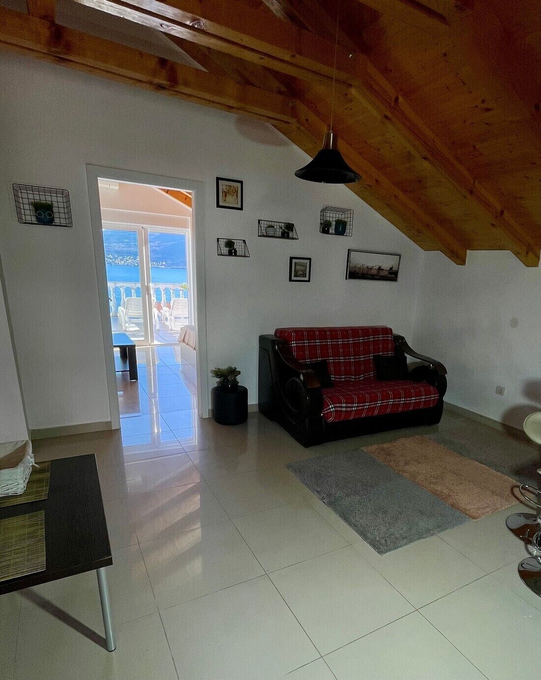 A living room with a red plaid sofa, a black coffee table, and a ceiling fan. There are several wall-mounted shelves with decorative items and a door leading to a balcony.