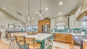 Una cocina amplia con una isla central, armarios de madera y electrodomésticos de acero inoxidable, además de iluminación colgante.