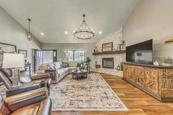 A spacious living room with a fireplace, leather sofas, a large rug, and a television on a wooden cabinet. - Hike, Golf, Ski & More! Spacious Ruidoso Home (Ruidoso)