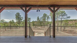 Una terraza de madera con barandilla de metal, que conduce a un área cubierta con vistas a un paisaje boscoso.