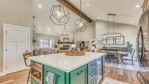 Una cocina amplia con una isla central, iluminación colgante y un comedor con mesa y sillas de madera.