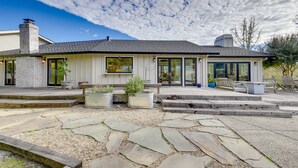 Ein modernes Haus mit einer Steinterrasse, Sitzgelegenheiten im Freien und einem großen Fenster mit Blick auf den Garten.