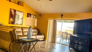 A living room with a brown leather sofa, a coffee table with a lamp, a TV stand, and a large window with curtains. - 3 bedroom/ 2 bath/ pool/ spa
Located in NE Cape Coral (Cape Coral)
