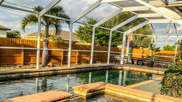 A covered swimming pool with a wooden fence and palm trees in the background. - 3 bedroom/ 2 bath/ pool/ spa
Located in NE Cape Coral (Cape Coral)