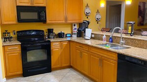 A kitchen with wooden cabinets, a black microwave, a stove, a dishwasher, and a patterned rug. - 3 bedroom/ 2 bath/ pool/ spa
Located in NE Cape Coral (Cape Coral)