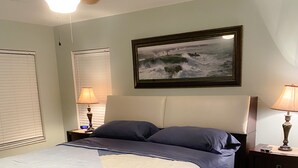 A bedroom with a bed, two bedside tables, a ceiling fan, a painting, and a window with blinds. - 3 bedroom/ 2 bath/ pool/ spa
Located in NE Cape Coral (Cape Coral)