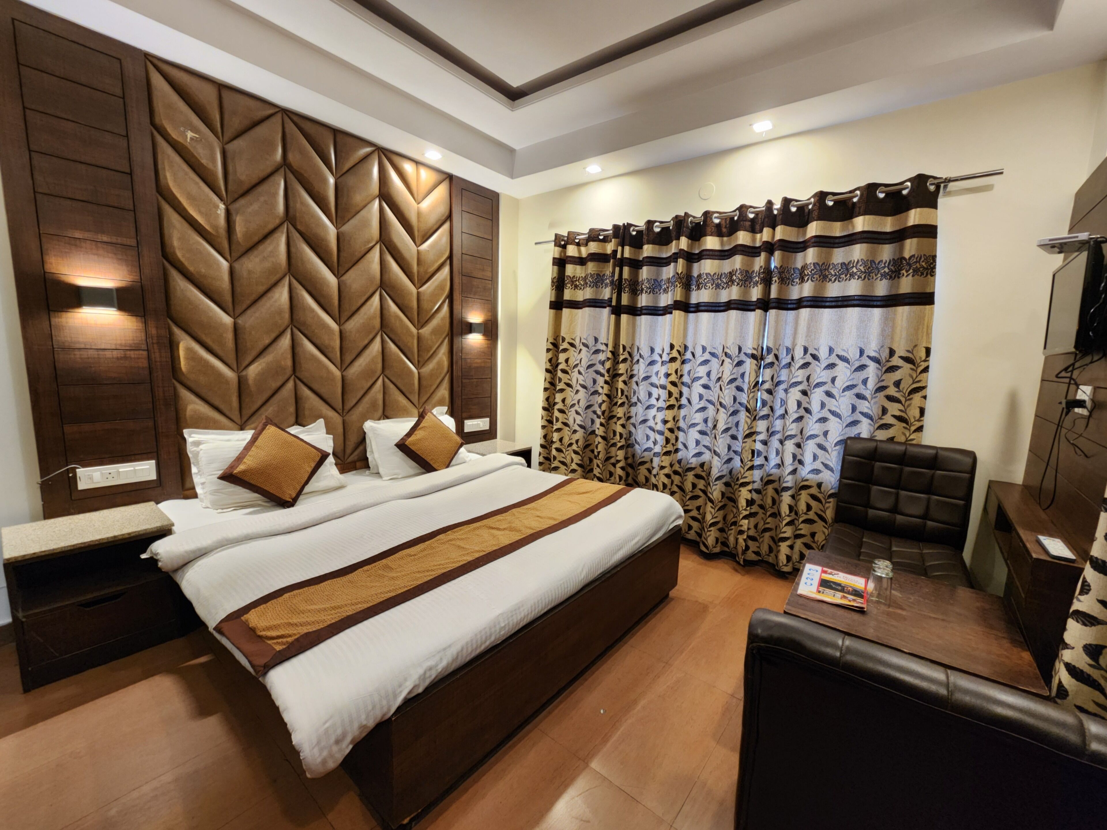 A modern hotel room with a large bed, a wooden headboard, a seating area with a table, and a television.