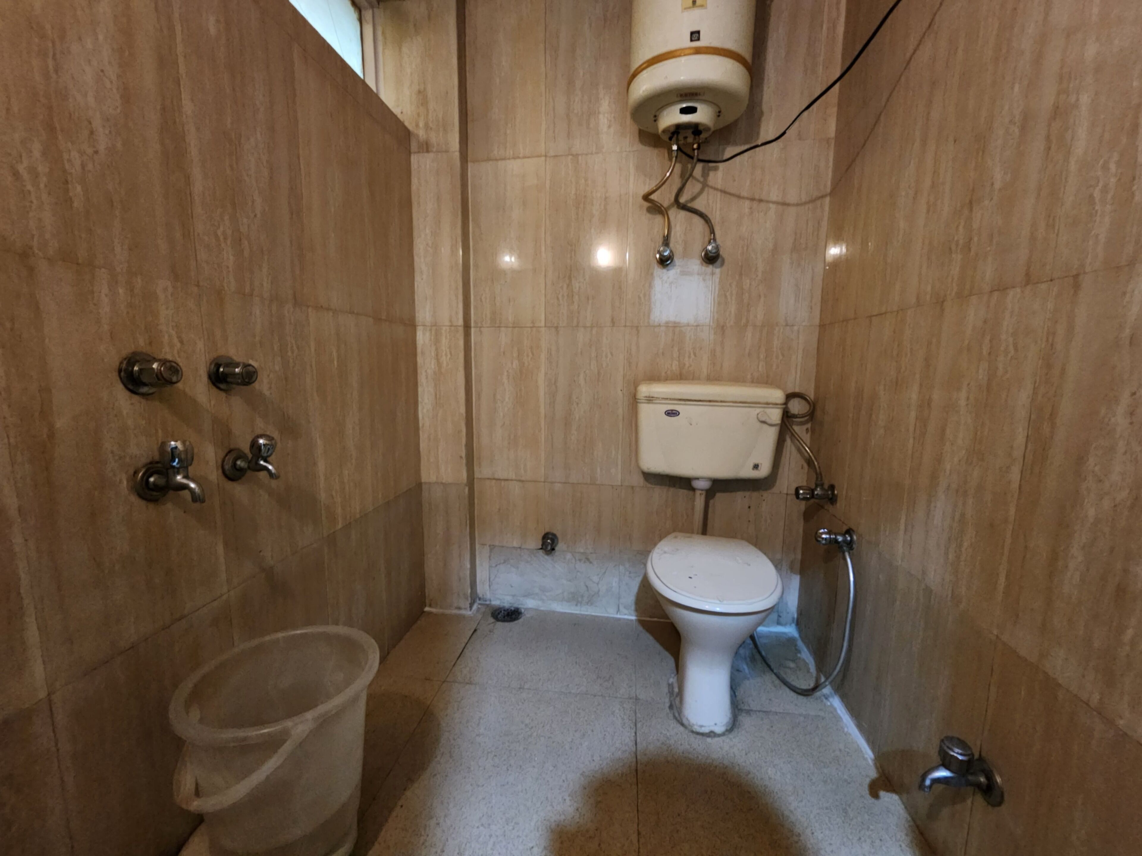 A small, tiled bathroom with a toilet, a bidet, a showerhead, and a water heater.