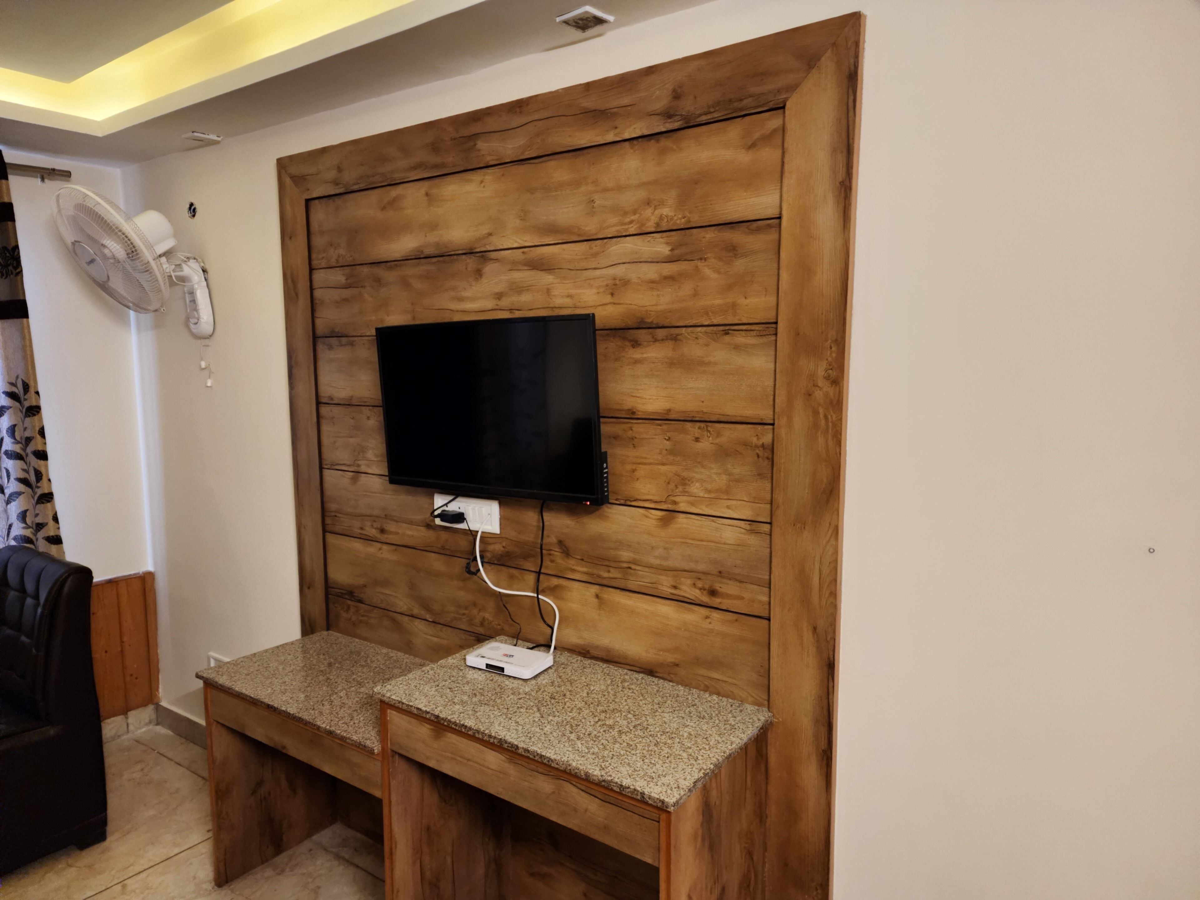 A room with a wooden wall panel design, a flat-screen TV mounted on it, and a small table with a power strip.