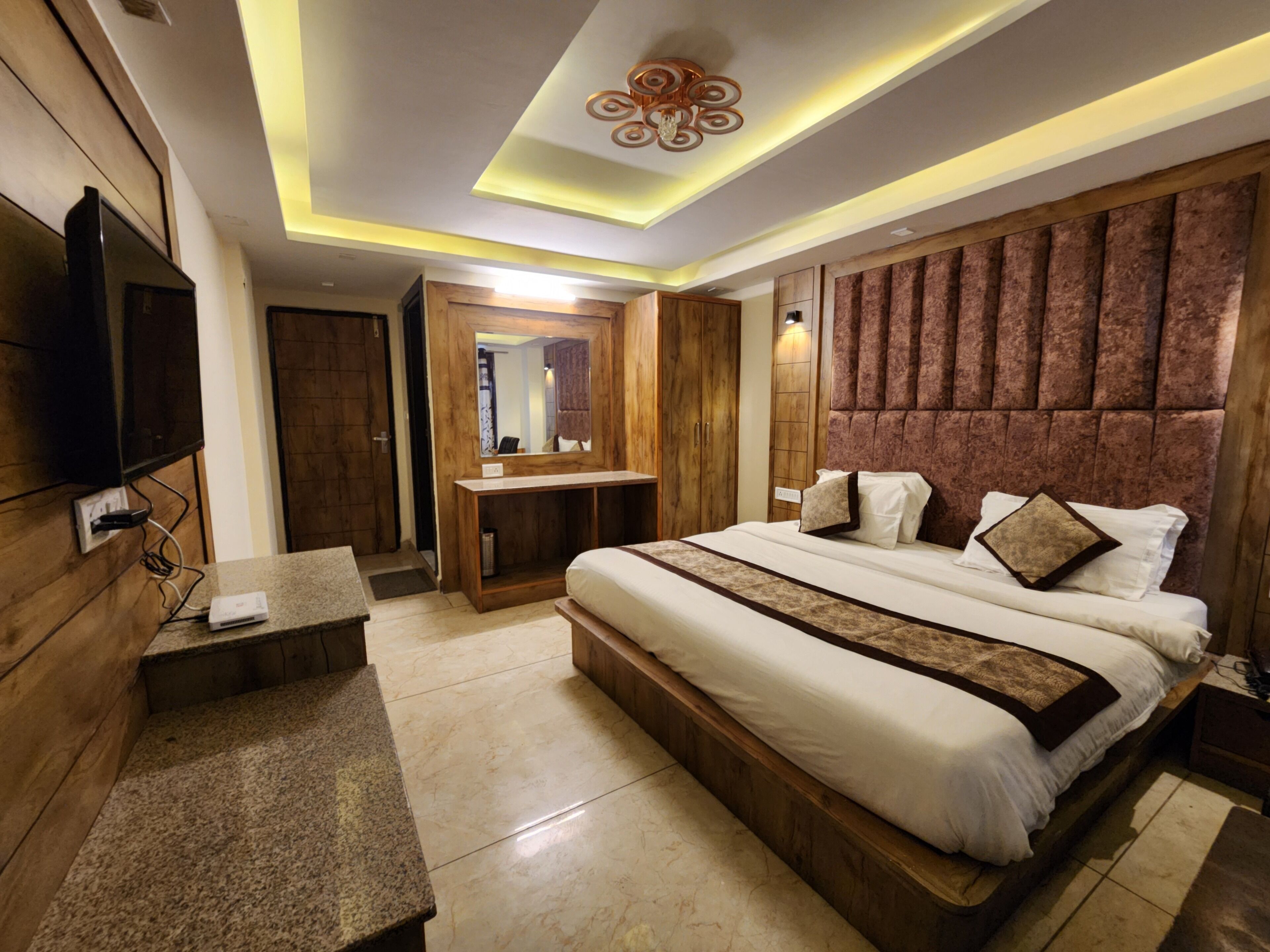 A modern bedroom with a large bed, wooden headboard, a flat-screen TV, and a vanity with a mirror.