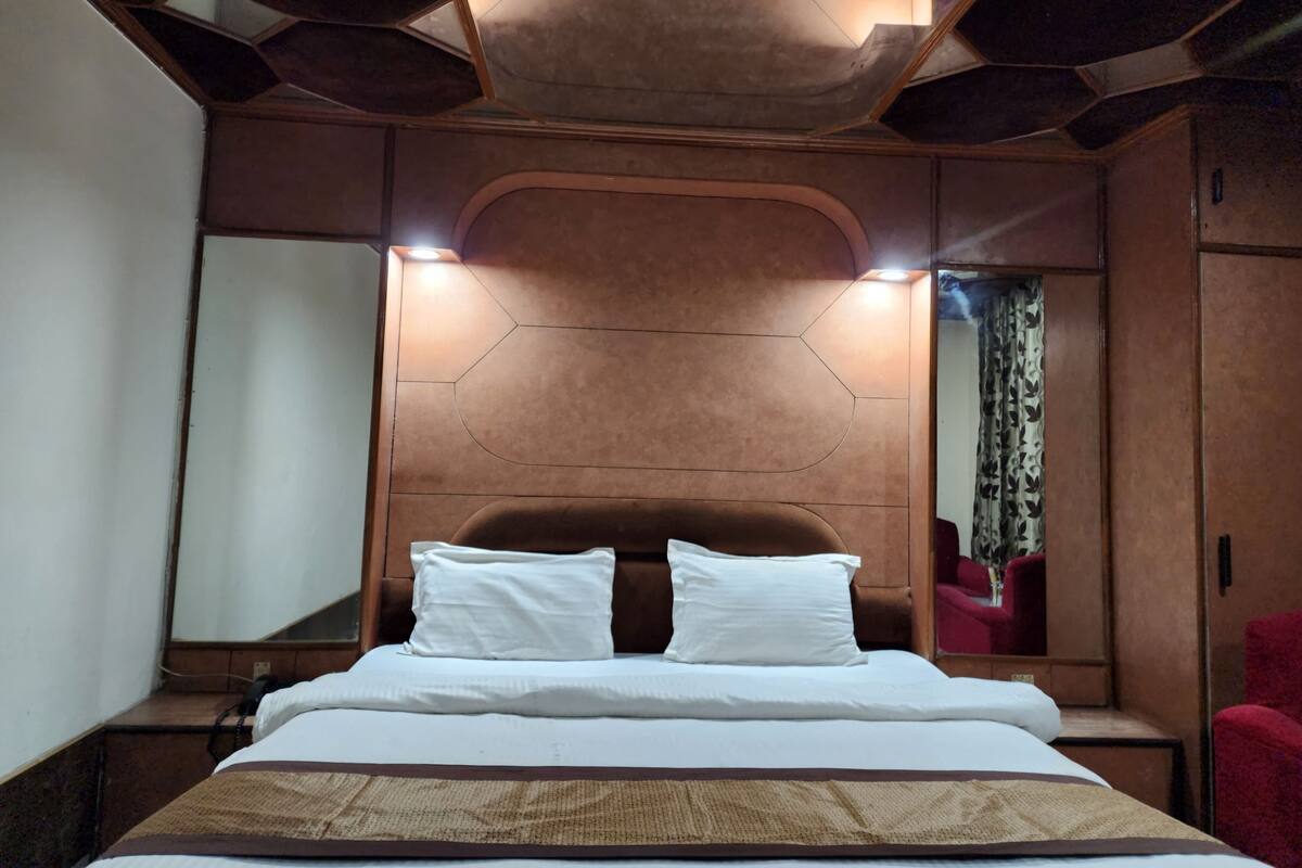 A modern hotel room with a geometric ceiling design, a large bed with white linens, and a red armchair.