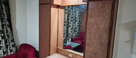 A room with a red armchair, a wooden cabinet with a mirror, and patterned curtains.