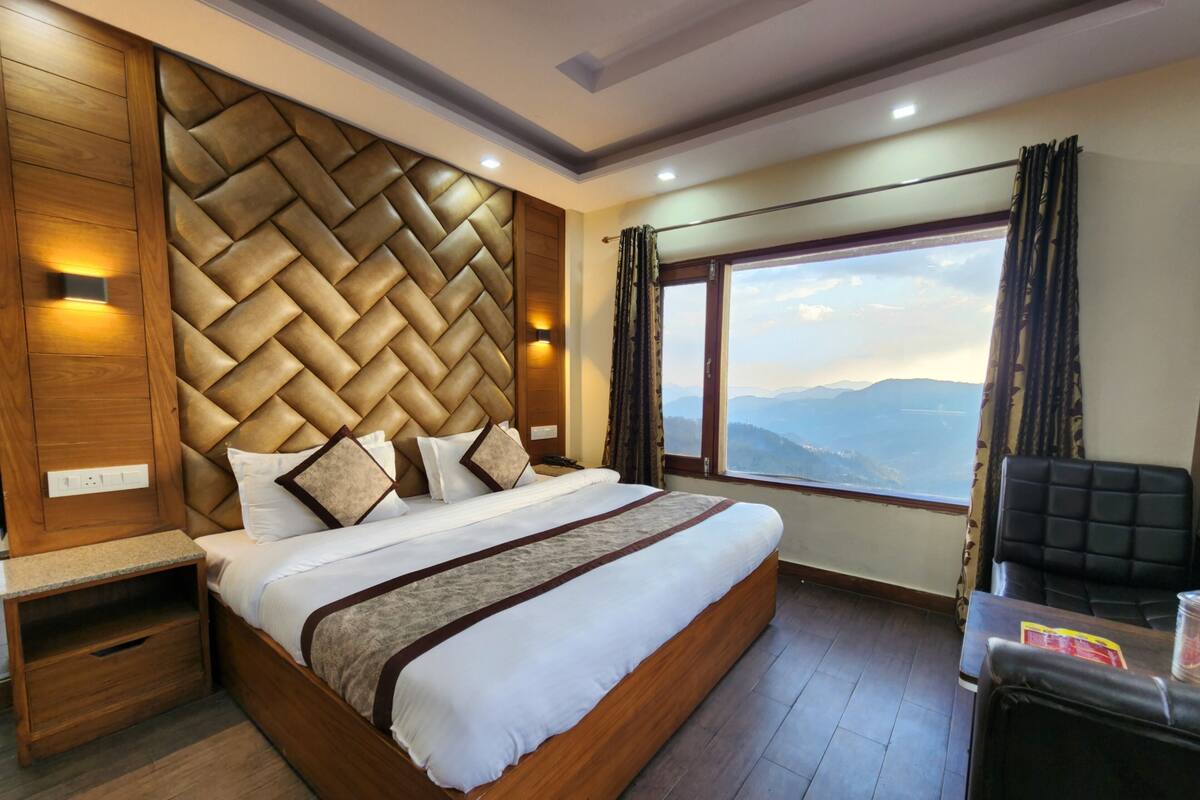 A modern hotel room with a large bed, wooden headboard, and a view of the mountains.