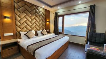 A modern hotel room with a large bed, wooden headboard, and a view of the mountains.