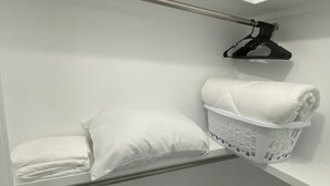 Een witte kast met een kledingroede, een opgevouwen wit kussen, en een witte wasmand.