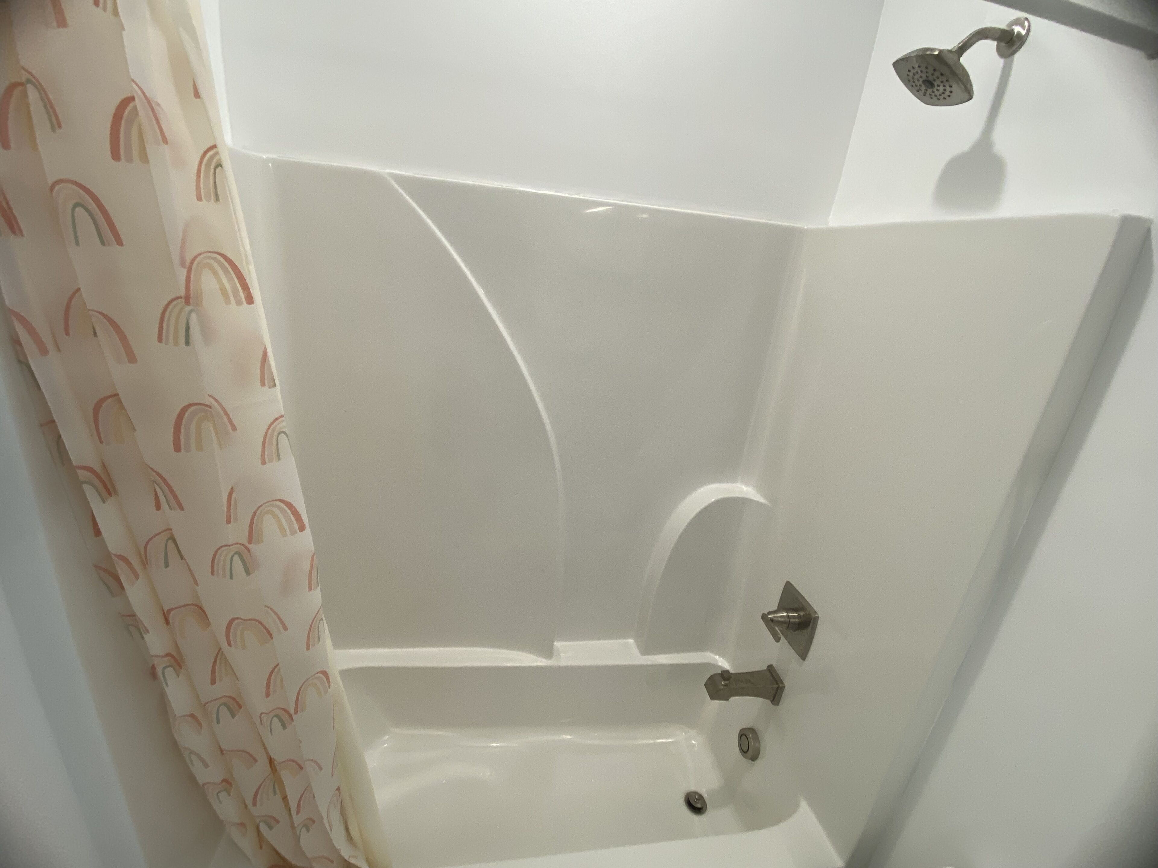 A bathtub with a showerhead, a curtain with a rainbow pattern, and a faucet.