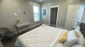 Een slaapkamer met een bed, bureau, stoel, deur en raam.