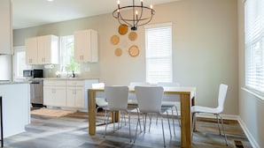 A modern kitchen with white cabinets, a dining table with four chairs, and a chandelier.