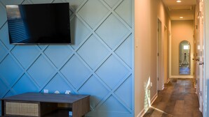 A modern living room with a flat-screen TV mounted on a blue geometric-patterned wall, a wooden entertainment unit, and a wooden floor.