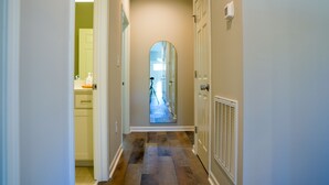 A hallway with a mirror reflecting a camera tripod, a door, and a vent on the wall.