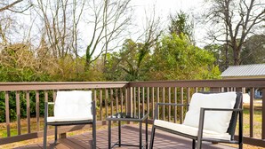 A wooden deck with two white cushioned chairs and a glass table.