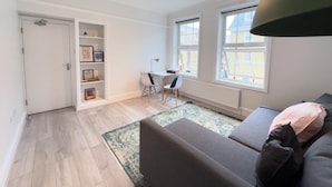 A modern living room with a grey sofa, a small desk, and a bookshelf. - The King's Cross Boutique Apartment!!! (London)