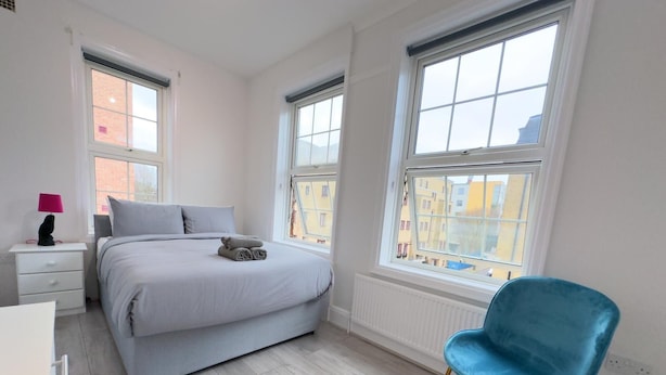 A bedroom with a bed, a chair, and a nightstand with a lamp. - The King's Cross Boutique Apartment!!! (London)