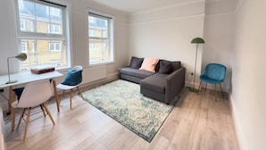 A modern living room with a grey sofa, a blue chair, a white desk with a lamp, and a patterned rug. - The King's Cross Boutique Apartment!!! (London)