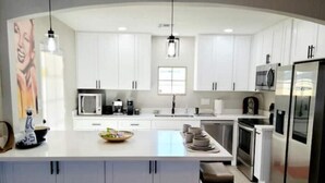 A modern kitchen with white cabinetry, a central island, a microwave, a refrigerator, and a sink. - Adorable Downtown Mesa Cottage (Mesa)