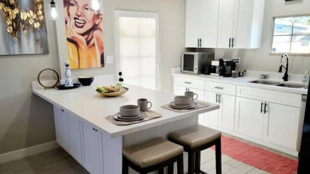 A modern kitchen with white cabinets, a central island with stools, a microwave, and a coffee maker. - Adorable Downtown Mesa Cottage (Mesa)
