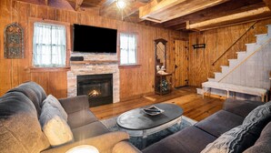 Una sala de estar acogedora con chimenea, paredes de madera, un televisor de pantalla plana y una escalera.