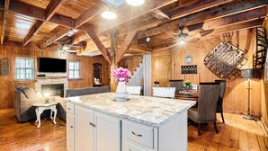 Interior acogedor de una cabaña con techo de madera, chimenea, comedor con sillas de mimbre y una isla grande con armarios.